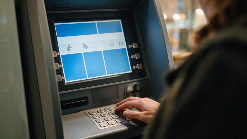 A hand on the keypad of a cash machine, the screen showing plain panels