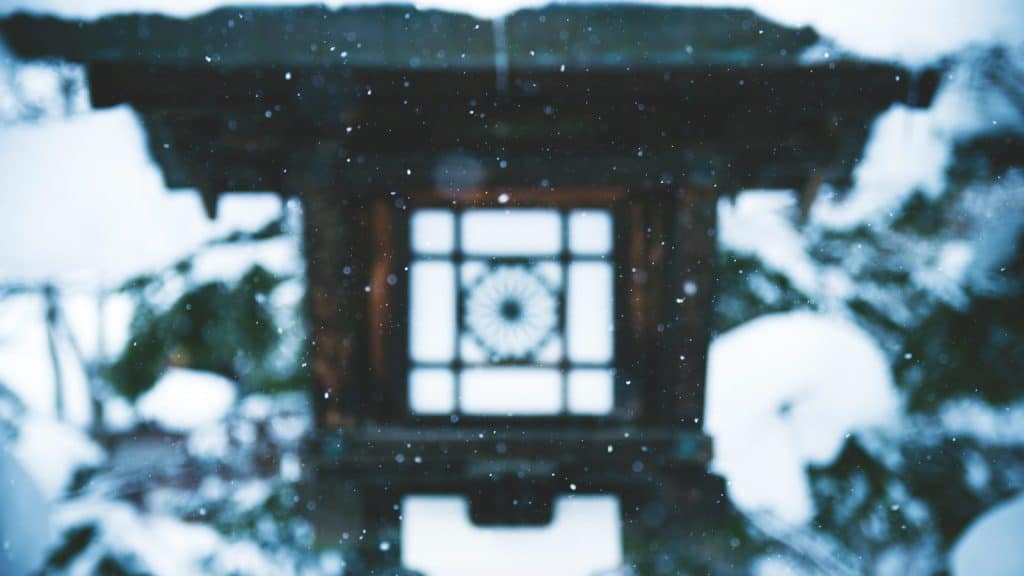 Snow falling around a stone lantern in a Japanese temple garden
