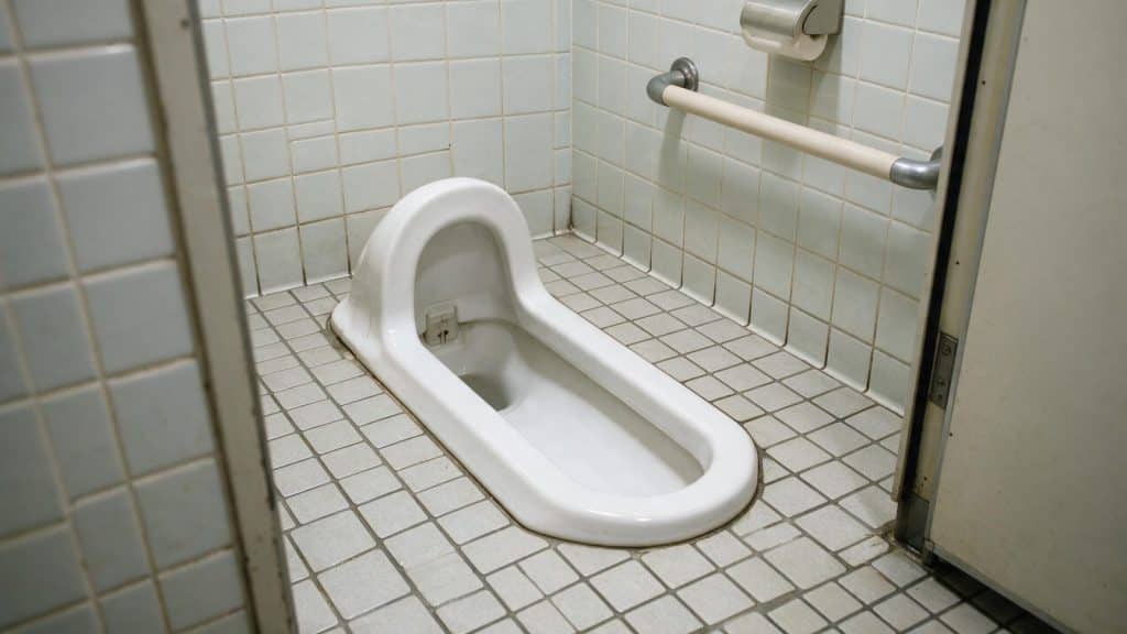 A traditional Japanese squat toilet set into the floor of a tiled cubicle