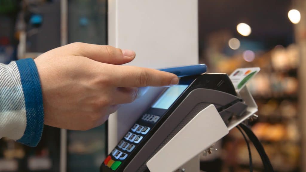 A hand holding a smartphone against a payment terminal