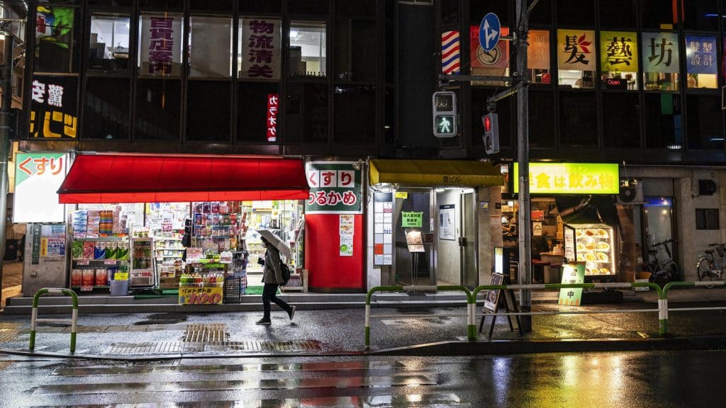 A Japanese shopping street with wet pavement reflecting shop signs