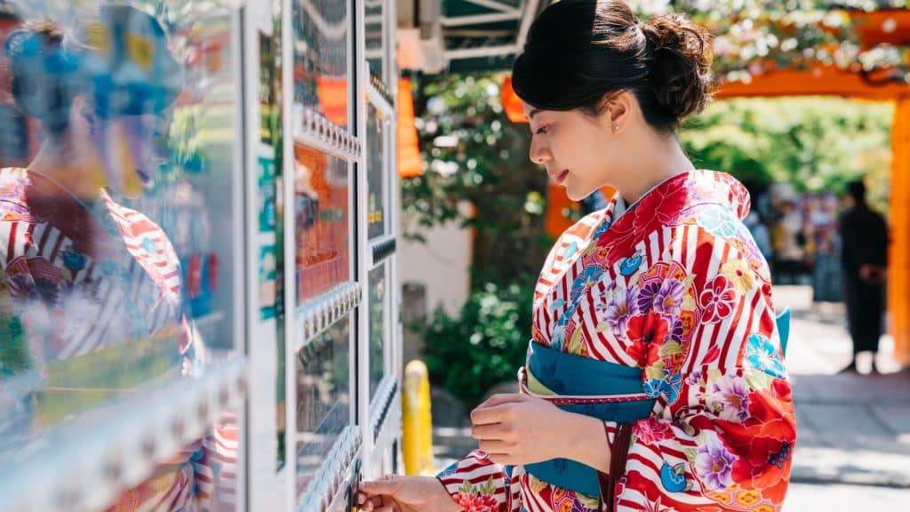 A woman in a kimono putting coins into a drinks vending machine in Kyoto