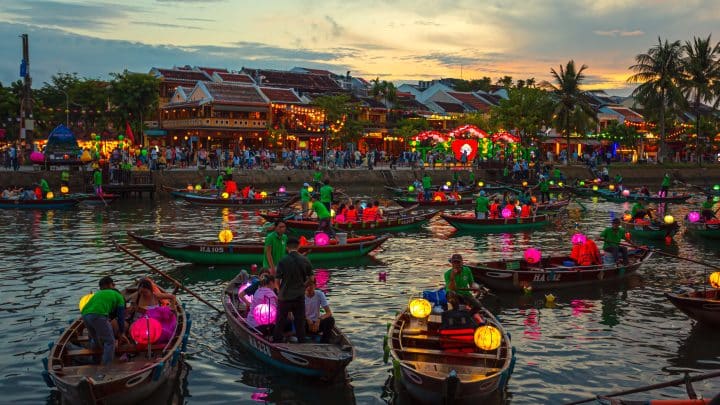 Yellow shophouses, boats and silk lanterns along the river in Hoi An old town at sunset