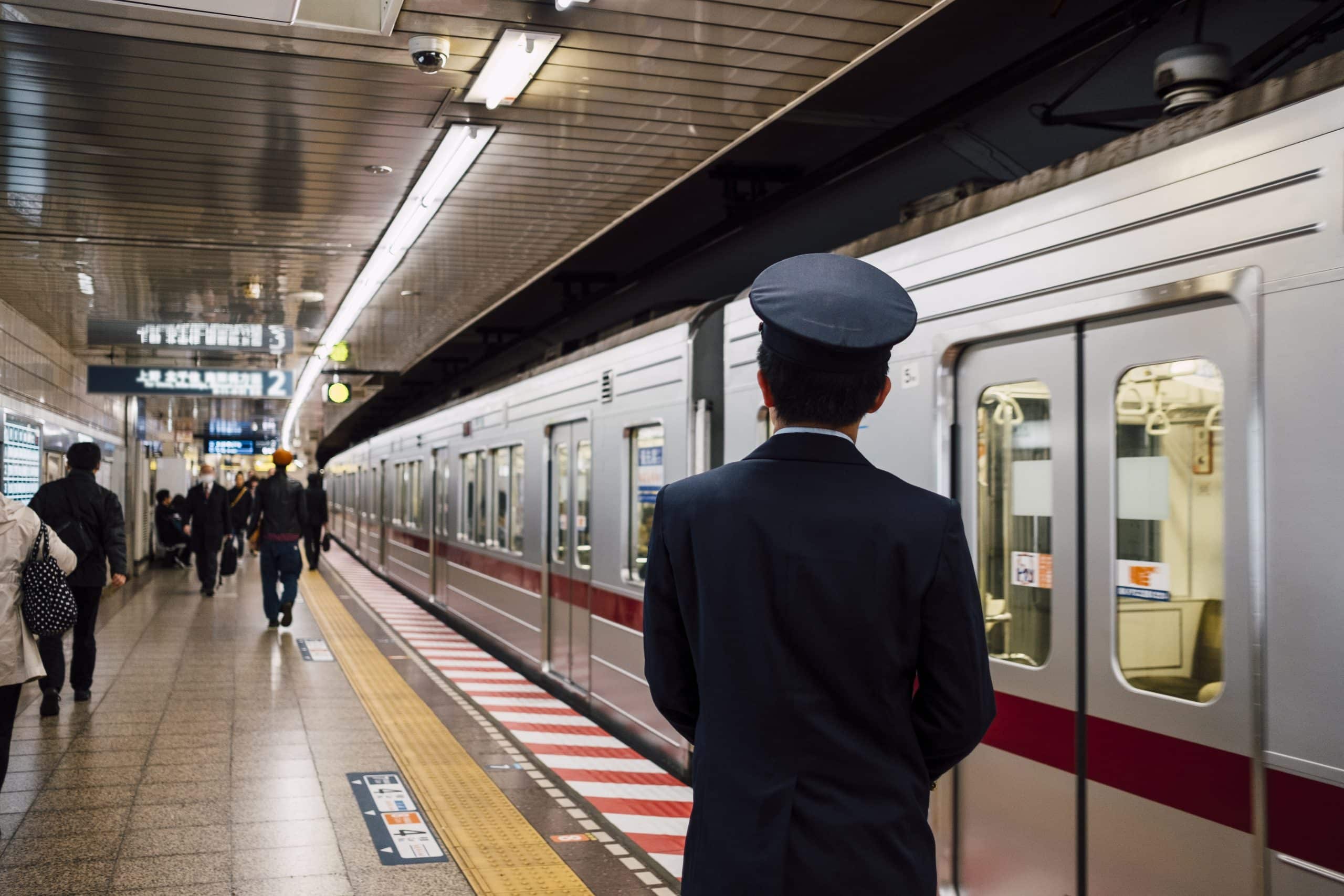 A uniformed railway staff member on a Japanese station platform