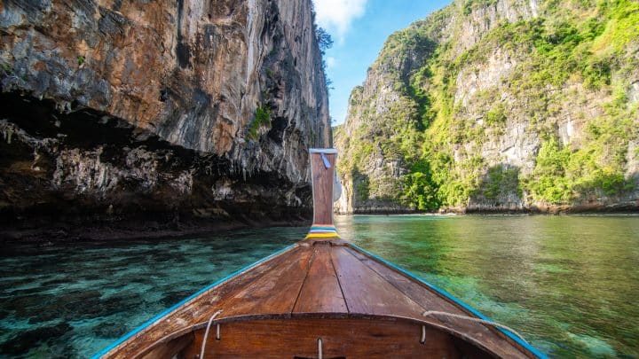 Bow of a wooden longtail boat decorated with ribbons at Maya Bay beach below limestone cliffs