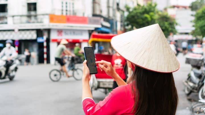 Tourist looking at a map on her mobile phone while walking in Hanoi, Vietnam