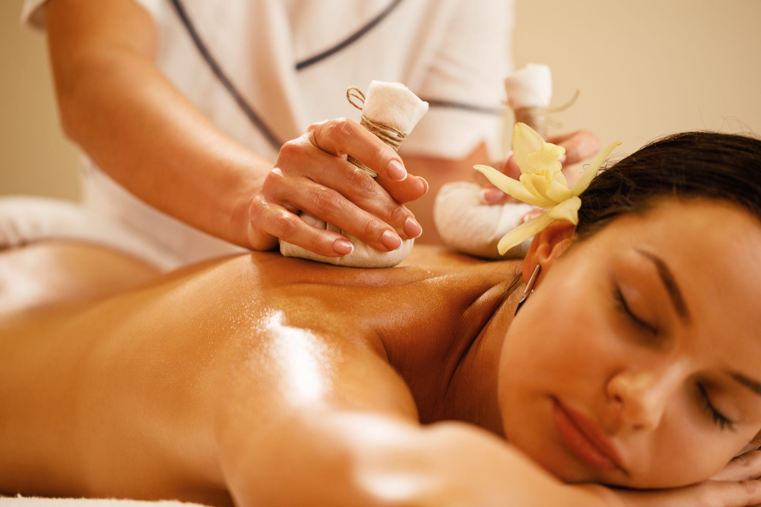 A therapist pressing Thai herbal compress balls on a client's back during a spa massage