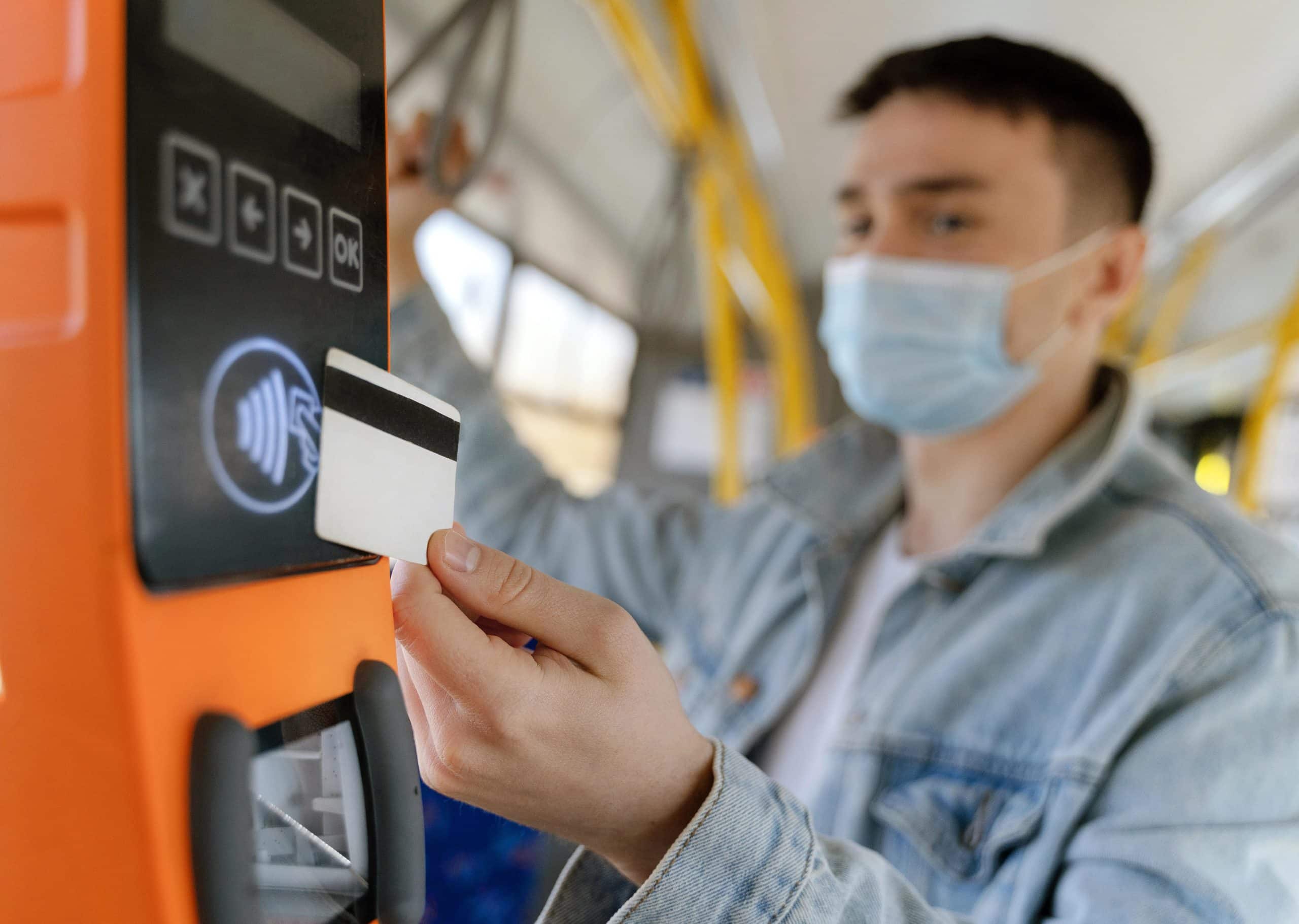 Young man paying his city bus fare with a transit card at the reader