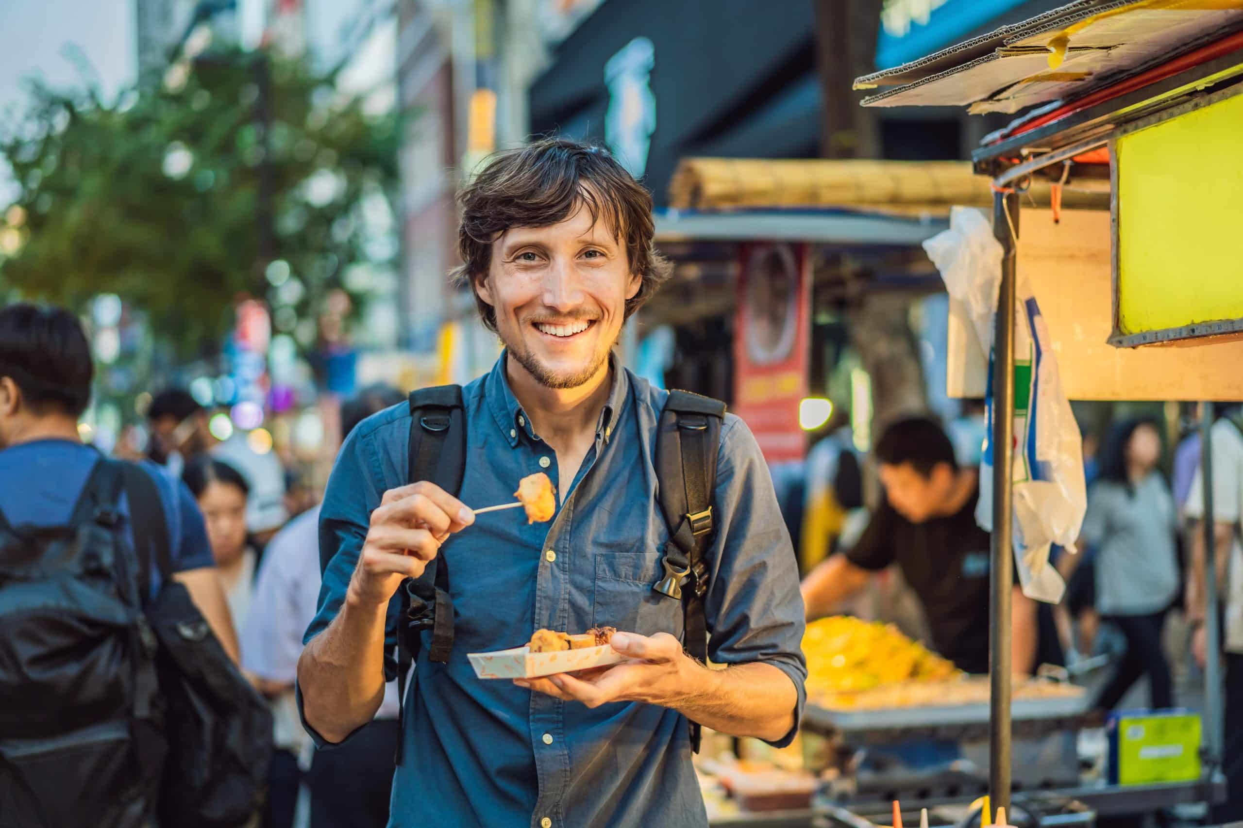 Traveler eating Korean street food on a busy street in Seoul
