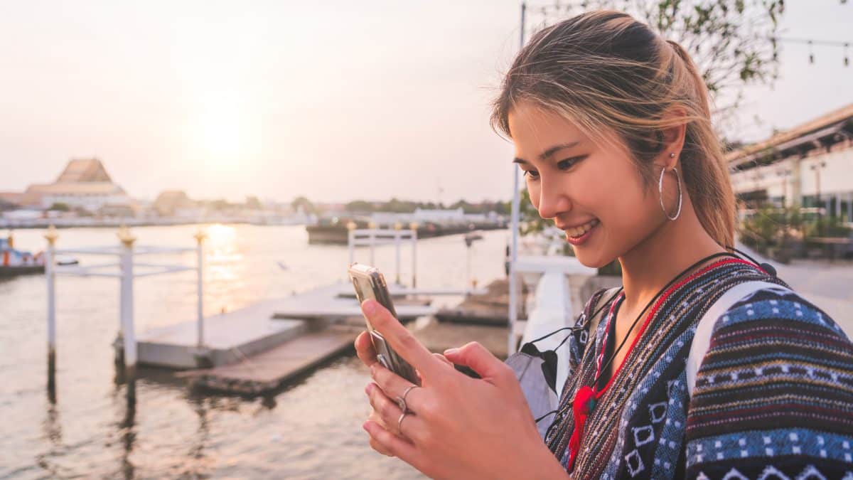 Traveler using her mobile phone by the Chao Phraya River in Bangkok at sunset