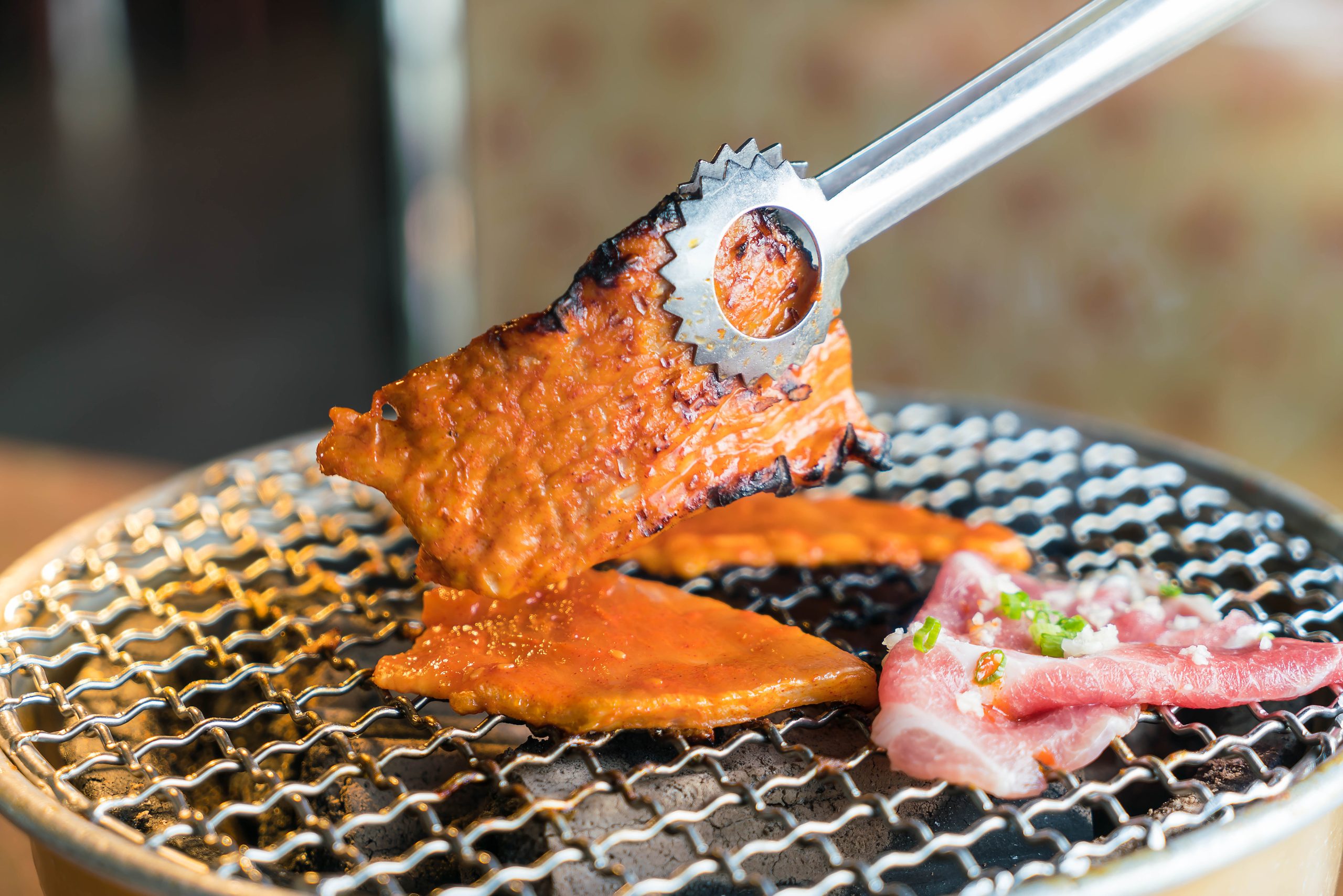 Slices of pork cooking on a charcoal grill at a Korean barbecue table