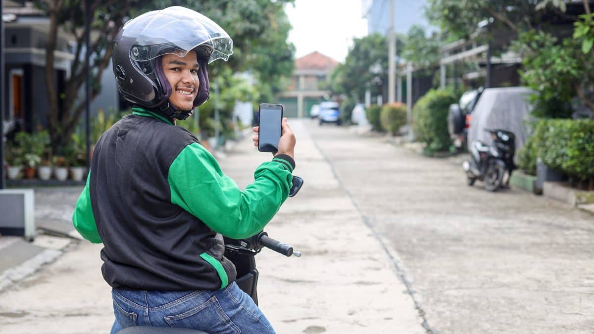 Ride-hailing motorbike driver in a green jacket and helmet holding a smartphone