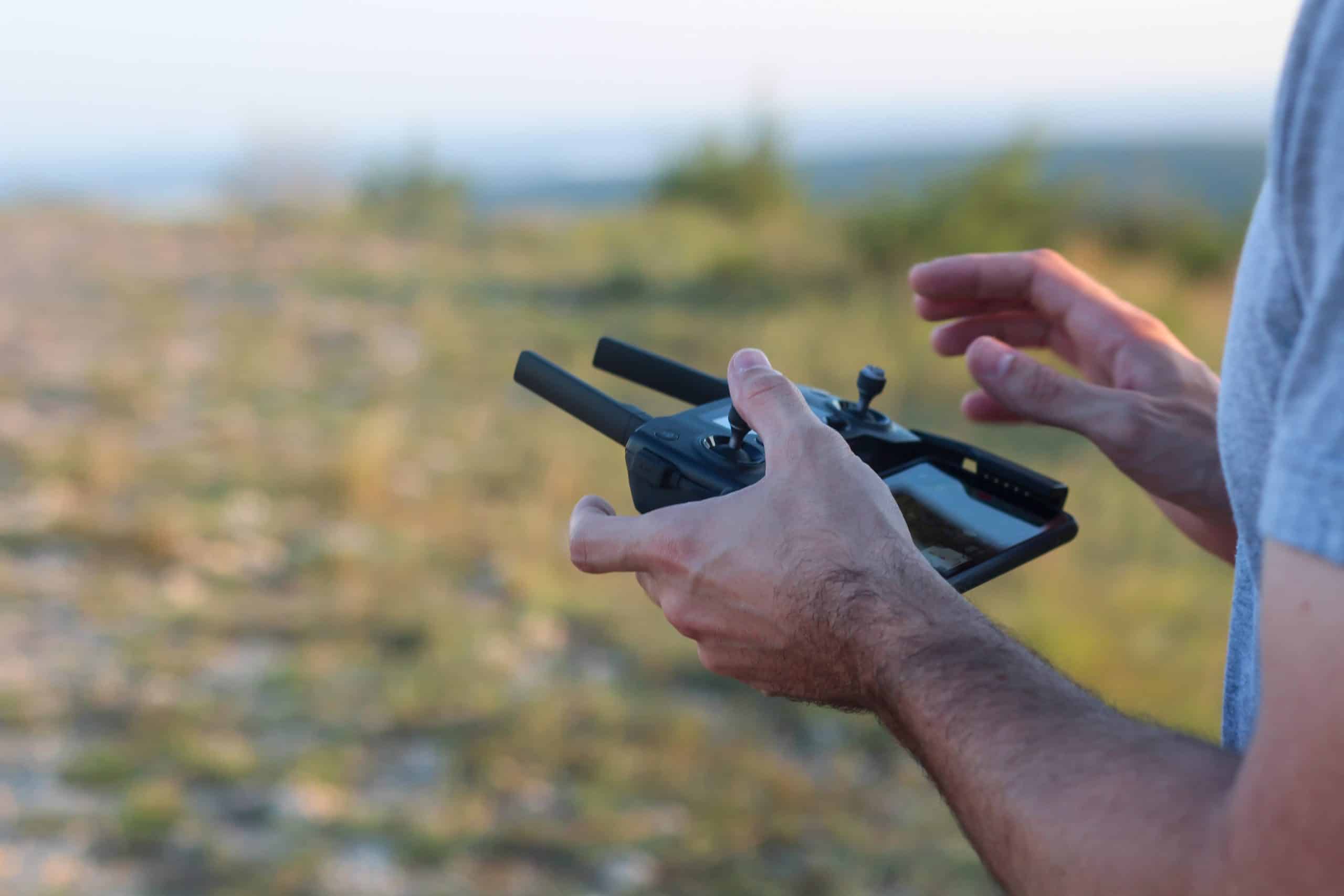 A person operating a consumer quadcopter drone outdoors with a handheld remote controller