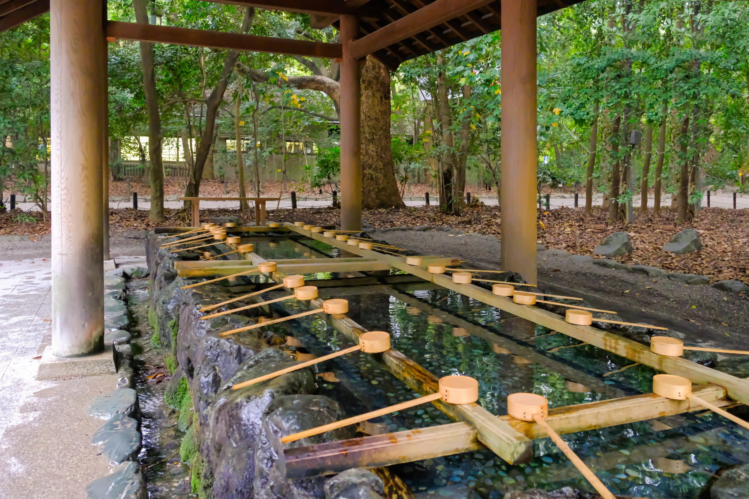 Visitors using bamboo-handled ladles to rinse their hands at a stone temizuya purification basin before entering a Japanese shrine