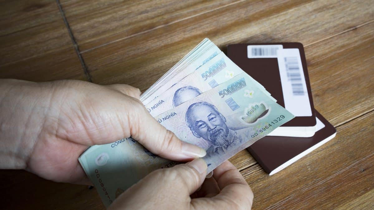 Hands counting Vietnamese dong banknotes next to a passport on a wooden table