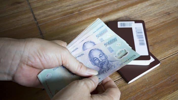 Hands counting Vietnamese dong banknotes next to a passport on a wooden table
