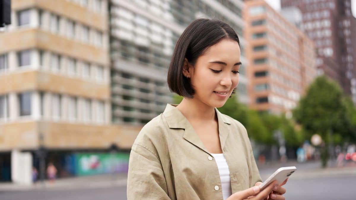 Young woman walking down a city street while looking at a map app on her phone
