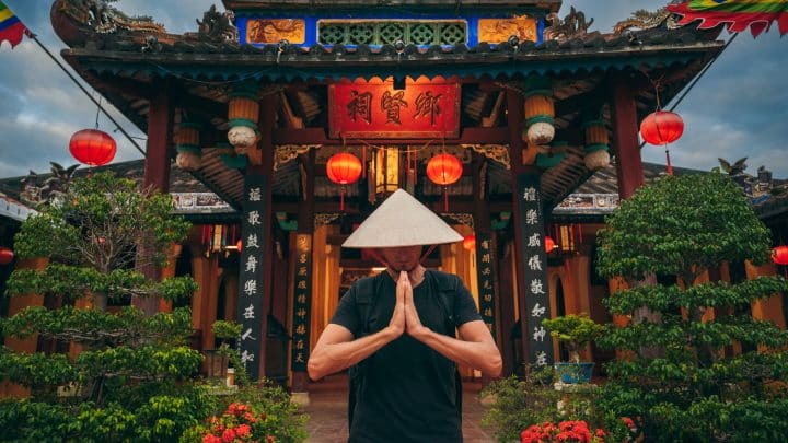 Male tourist in a Vietnamese non la hat praying at a Buddhist pagoda in Hoi An, Vietnam