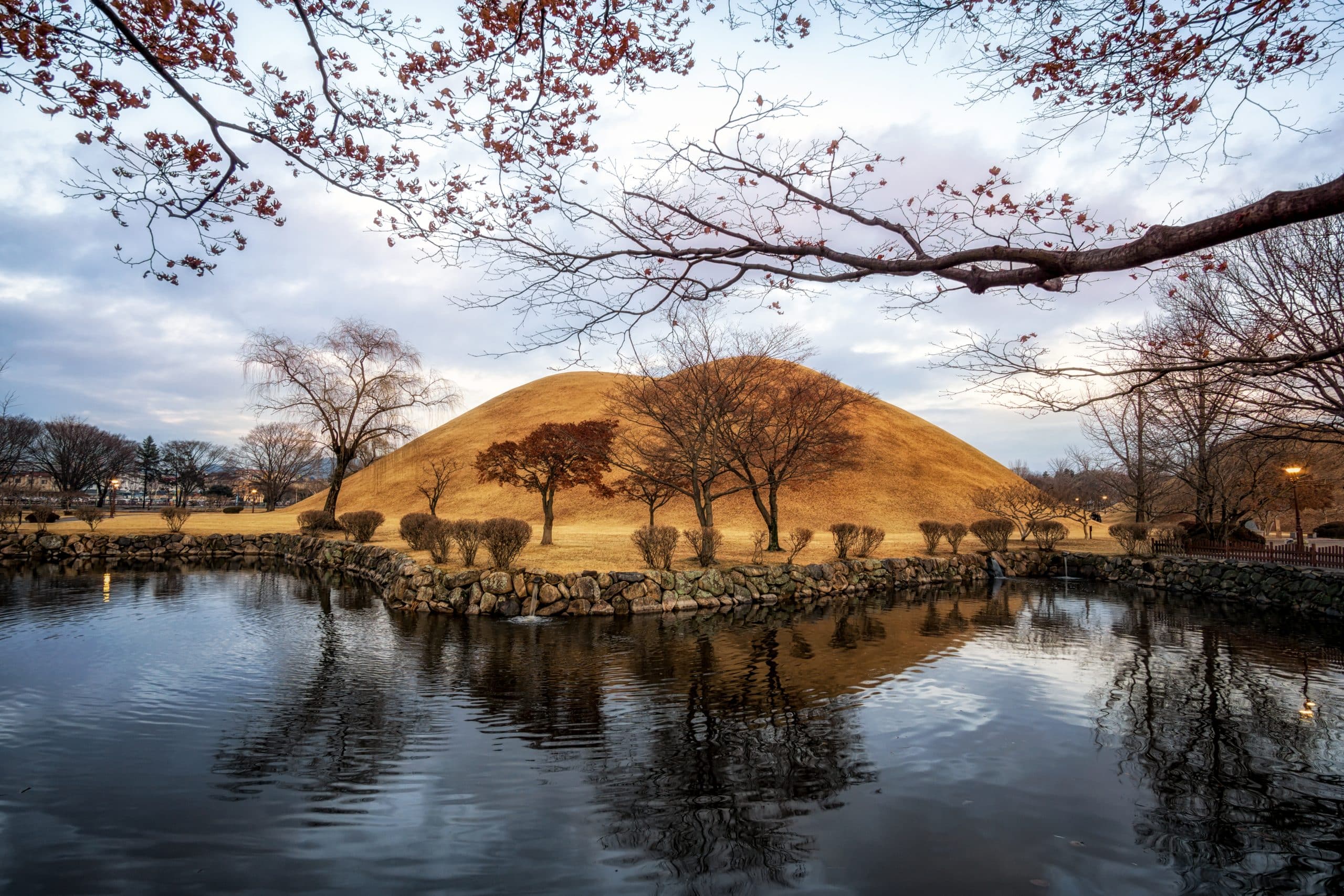 Grass-covered Silla royal tomb mounds reflected in a small pond at Daereungwon in Gyeongju