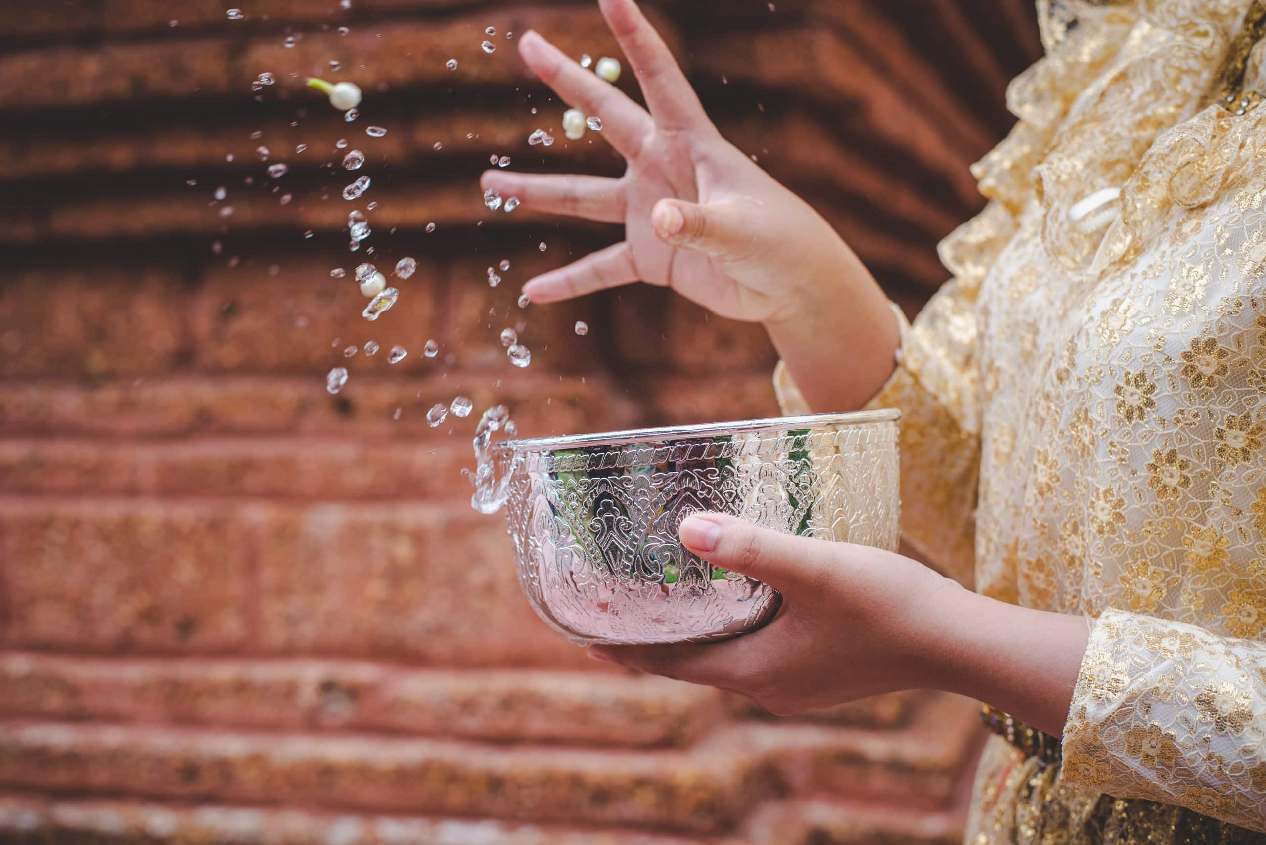 Close-up of a hand holding a bowl of water during a Songkran festival ceremony at a Thai temple
