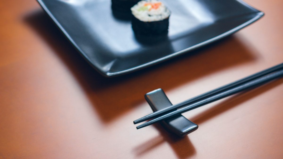 A pair of chopsticks resting horizontally on a ceramic hashioki chopstick rest next to a plate of sushi