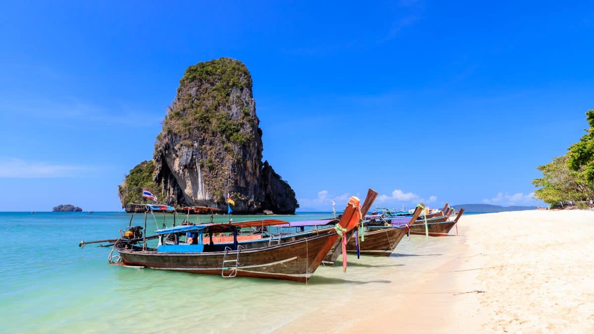 Longtail boat on turquoise water below limestone cliffs at Phra Nang Beach, Krabi